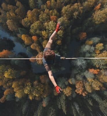 Person mit roten Handschuhen balanciert auf einem Seil über herbstlich gefärbtem Wald um die Resilienz zu trainieren